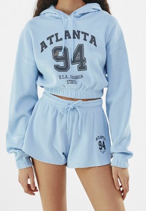 Completo loungewear blu chiaro a coste, composto da un hoodie corto con la scritta "ATLANTA 94" e "U.S.A. Georgia State", abbinato a pantaloni corti con vita elastica.