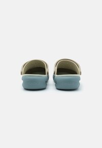Lightweight clogs in cream and blue. Features ventilation holes, molded design, and textured footbed, with branding on the back.