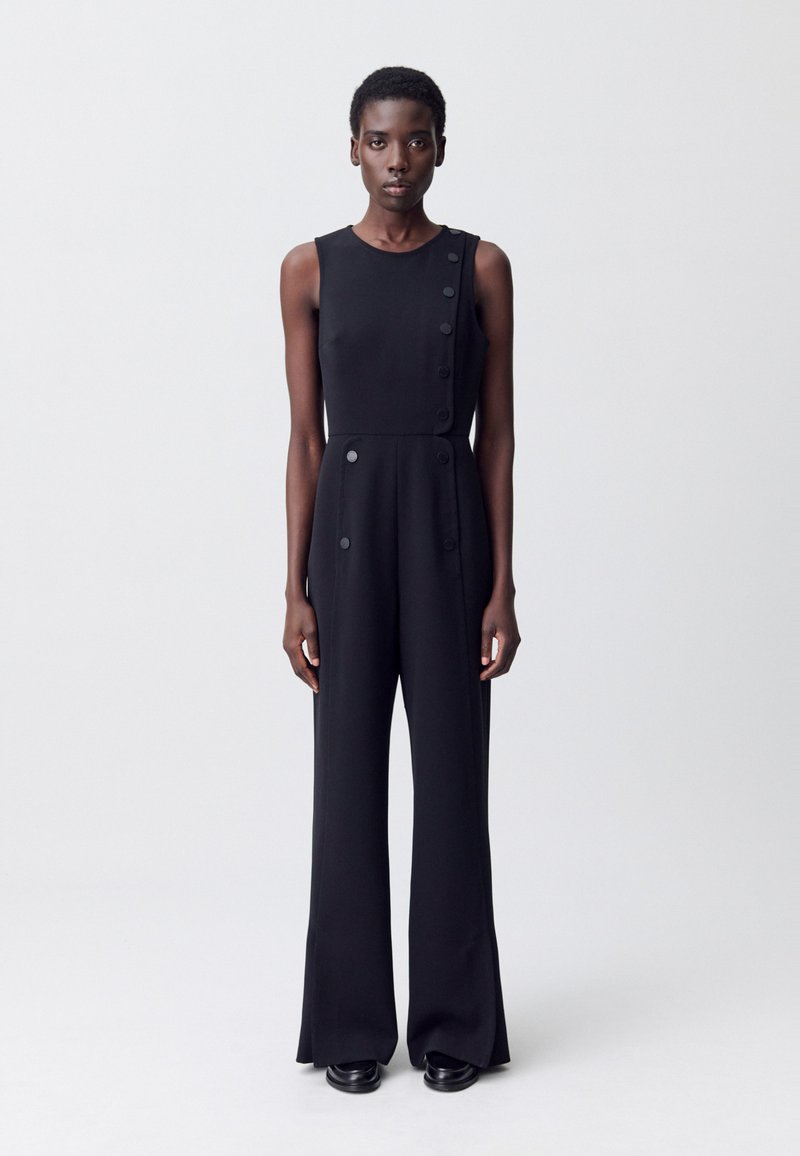 Combinaison noire sans manches avec un buste ajusté, des jambes évasées et des accents de boutons sur les côtés. Tissu lisse avec une finition mate.