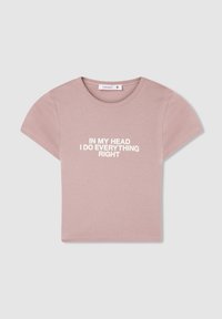 Maglietta rosa chiaro realizzata in tessuto morbido, con maniche corte e scollo rotondo. Il testo recita "Nella mia testa faccio tutto giusto" in bianco.