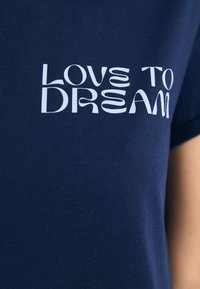 Mörkblå t-shirt i bomull med vit text som säger "LOVE TO DREAM" i ett modernt, konstnärligt typsnitt.