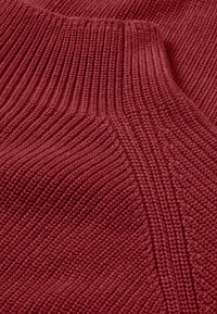 Tessuto a maglia color marsala con texture ribbata e motivi diagonali, caratterizzato da una composizione morbida e spessa. Linee di cucitura chiare visibili.