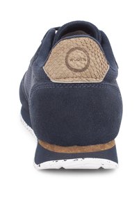 Marineblauer Sneaker mit einem strukturierten Holzfersenakzent und einem Obermaterial aus Wildleder, ausgestattet mit einer weißen, gesprenkelten Außensohle. Sechseckiges Design an der Rückseite.