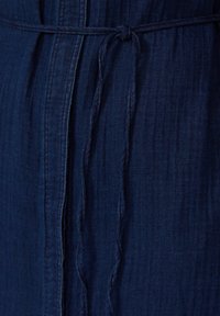 Tessuto denim blu navy con superficie testurizzata, caratterizzato da una cintura legata e dettagli di cucitura verticale per una maggiore struttura.
