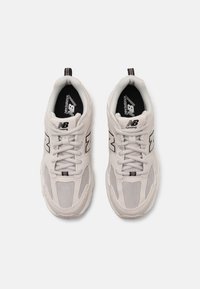 Baskets de course gris clair en mesh et matériaux synthétiques, avec des accents noirs et un logo distinct "N" sur les côtés.