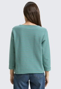 Striped long-sleeve top in teal and white cotton blend, featuring a boat neckline and relaxed fit, paired with blue denim jeans.