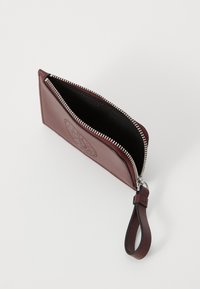 Portafoglio in pelle bordeaux con chiusura a zip argentata, caratterizzato da un design impresso sulla parte frontale e un interno in tessuto nero. Include un cinturino da polso.