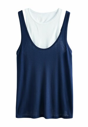 Ribbede ærmeløs tanktop lagdelt over en hvid ærmeløs skjorte, begge med rund halsudskæring, navyblå yder og hvid inder.