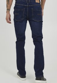 Tamno plave traperice slim kroja, s dva stražnja džepa, kontrastnim šavovima i kožnom oznakom na struku.