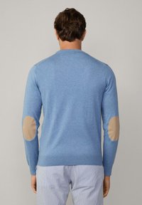 Jasnoniebieski wełniany sweter z długimi rękawami, z tanowymi łatami na łokciach, okrągłym dekoltem oraz ściągaczami przy rękawach i u dołu.