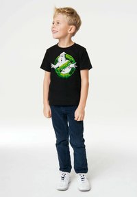 Black cotton t-shirt featuring a graphic of a ghost with green accents. Paired with navy blue pants and white sneakers.