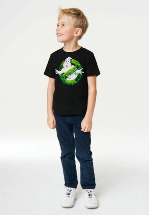 Schwarzes Baumwoll-T-Shirt mit einem Grafikdesign eines Geistes in grünen Akzenten. Kombiniert mit marineblauen Hosen und weißen Sneakers.