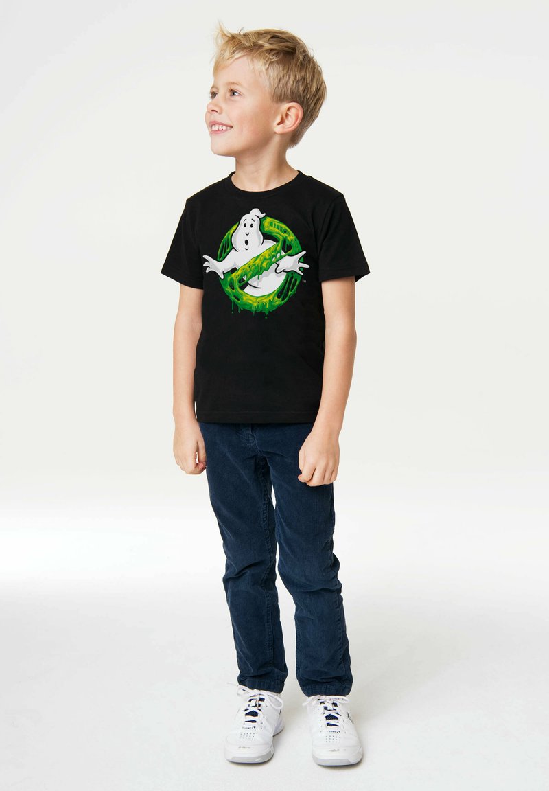 Black cotton t-shirt featuring a graphic of a ghost with green accents. Paired with navy blue pants and white sneakers.