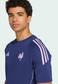 Marine sports t-shirt med lyserøde striber på skuldrene, har et haneemblem på brystet, lavet af åndbart stof.