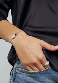 Silverarmband med en texturerad hänge och slät droppformad accent, i kombination med en matchande ring. Båda har en stilren, minimalistisk design.