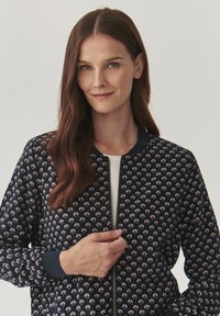 Cazadora bomber de la marina con patrón floral, tela texturizada, puños acanalados y cierre con cremallera. Presenta un cuello redondo y acentos vibrantes.