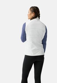 Biała ocieplana kamizelka z wysokim kołnierzem, zestawiona z niebieską bluzką z długim rękawem i czarnymi legginsami. Gładka faktura, sportowy design.