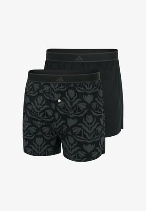 Dwie pary czarnych szortów bokserskich. Jedna ma ciemny wzór kwiatowy, podczas gdy druga jest jednolicie czarna. Obie mają elastyczny pas.
