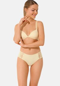 Un ensemble de lingerie jaune clair comprenant un soutien-gorge rembourré avec des bretelles en dentelle et un short taille haute assorti avec des accents en dentelle sur les côtés.