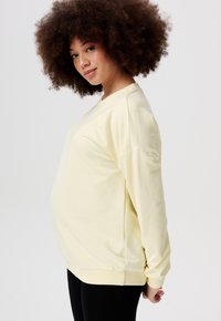 Lichtgele sweatshirt met een ronde halslijn en ingezette schoudernaden, gecombineerd met zwarte leggings; voorzien van een zachte textuur en een relaxte pasvorm.