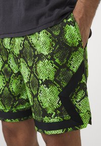 Σορτς με μοτίβο δέρματος πράσινου φιδιού και μαύρη ζώνη με λεπτομέρειες. Η υφή μιμείται τις κλίμακες, παρουσιάζοντας σχέδιο σε σχήμα διαμαντιού.