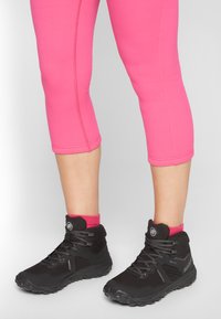 Botas de senderismo negras con tela texturizada, suelas de goma y cordones grises, usadas con leggins cortos rosas y calcetines a juego.