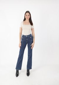 Top de manga corta beige con escote cuadrado, combinado con pantalones de denim azul de cintura alta y botas de tacón negro con punta.