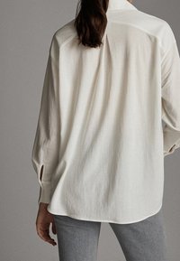 Långärmad, lös passform skjorta i ljus krämfärgad tyg. Har en rak baksida, sidospår och en klassisk kragsdesign.