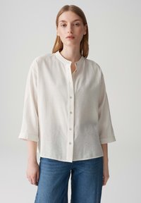 Camicia button-up di colore crema chiaro con colletto alla mandarina, maniche a tre quarti e taglio rilassato; realizzata in morbido tessuto testurizzato.