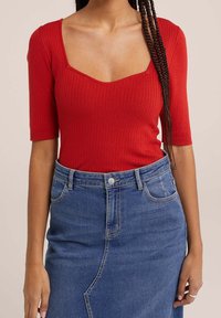 Roter gerippter Body mit quadratischem Ausschnitt und kurzen Ärmeln, kombiniert mit einem hoch taillierten Jeansrock mit einer Vordernaht und Taschen.