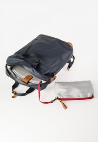 Zaino blu con dettagli in pelle marrone, dotato di un interno foderato e di un piccolo sacchetto grigio con una cerniera rossa e un motivo a griglia.