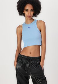 Lichtblauwe ribbelcrop-top met een ronde halslijn en een klein logotag, gecombineerd met zwarte, textuurachtige, elastische broeken met hoge taille.