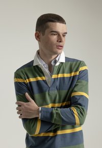 Camisa polo de manga larga a rayas verdes, azules y amarillas con cuello blanco, que presenta una tapeta con botones y una textura suave.