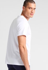 Witte T-shirt met korte mouwen te zien op een model, met een ronde hals en een relaxte pasvorm, gemaakt van een zachte katoenen stof.