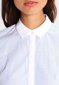Light blue and white striped shirt with a button-up collar, showing a smooth texture and a placket with a single button closure.