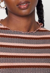 Strikket top med pink, brun og marineblå striber i et struktureret mønster. Volangkant ved halsen og korte ærmer tilføjer detaljer.