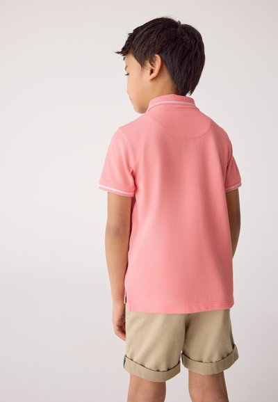 Polohemd in koraalroze met korte mouwen en witte accenten, gecombineerd met beige korte broek. Soepele textuur, casual pasvorm, zichtbare kraag.