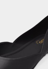 Chaussure plate noire à bout pointu avec bord festonné et semelle intérieure rembourrée, en matériau lisse.