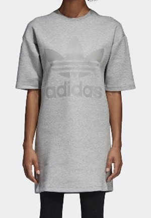 Person iført en løs grå kortærmet kjole med et stort Adidas-logo foran, kombineret med sorte leggings.