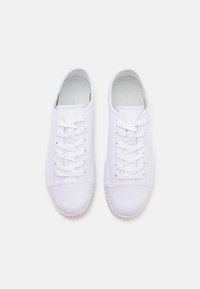 Par av rena vita canvas-sneakers med snörning, sedda ovanifrån på en ljus bakgrund.