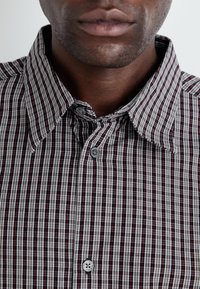Button-up shirt featuring a red, black, and white plaid pattern, with a structured collar and grey button details.