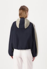 Marinblå och beige tvåfärgad huva-jacka, elastiska muddar och kant, lättviktig tyg, avslappnad passform, har snörning vid nederkanten.