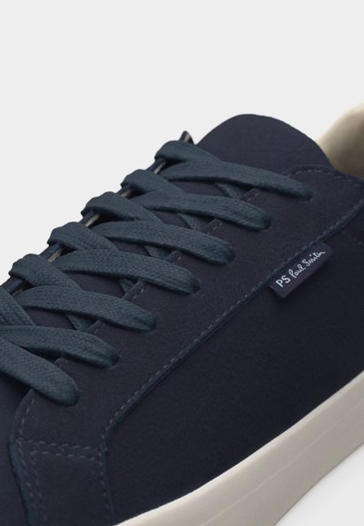 Αθλητικό παπούτσι από μπλε ναυτικό σουέντ με κορδόνια στο ίδιο χρώμα, λευκή σόλα και μικρή υφασμάτινη ετικέτα "PS Paul Smith" στο πλάι κοντά στα κορδόνια.