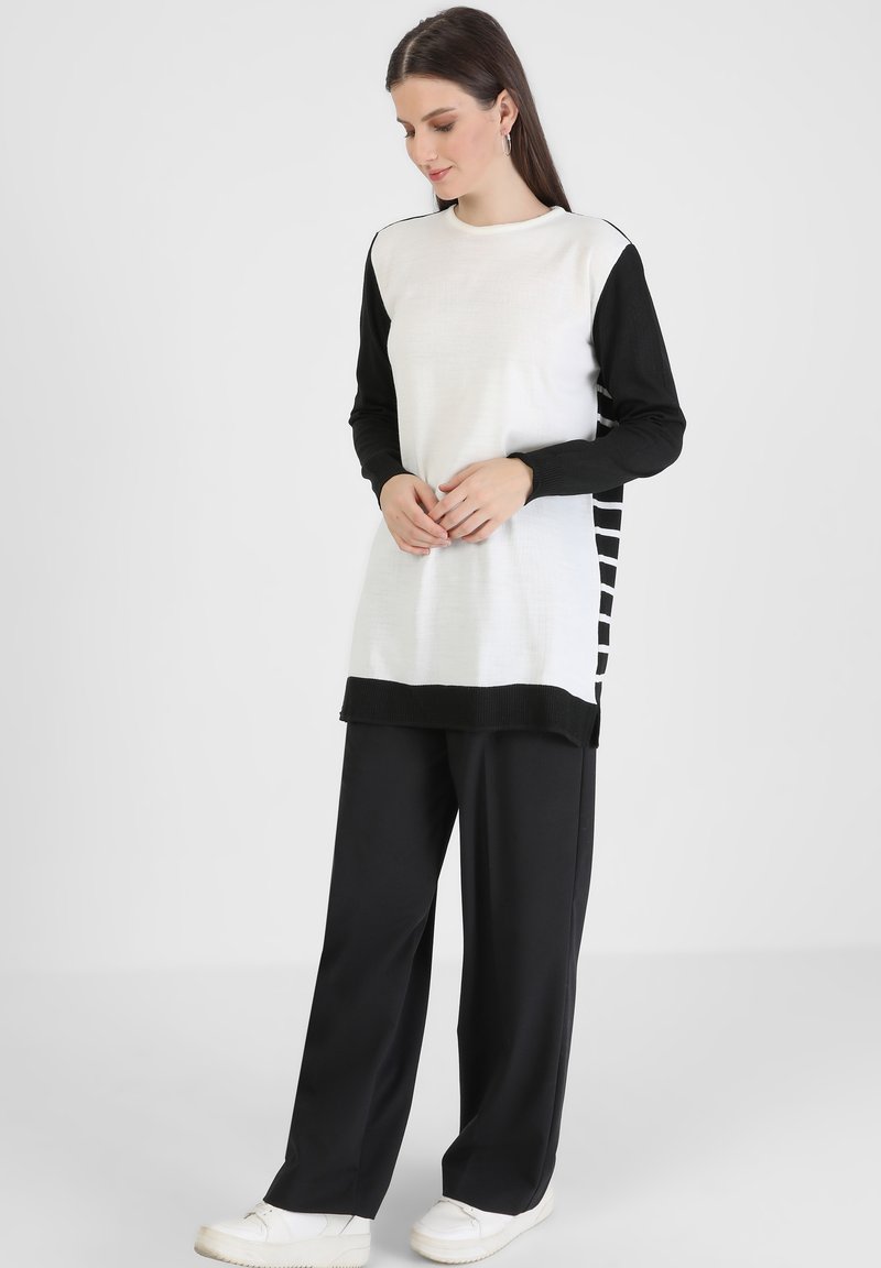 Maglietta a maniche lunghe con maniche nere e corpo bianco finitura testurizzata; abbinata a pantaloni neri larghi e sneakers bianche.