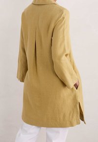 Leinen langer Mantel in Hellgelb mit Kragen, seitlichen Taschen und einem Rückenfalten für mehr Bewegungsfreiheit. Verfügt über lange Ärmel und einen geraden Schnitt.