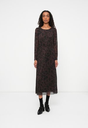 Durchscheinendes schwarzes Kleid mit einem Leopardenmuster, langen Ärmeln, runder Halslinie und tailliertem Schnitt, getragen mit schwarzen High Heels und Socken.