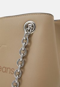 Beige faux læder tote taske med sølv metal øje og kæde detalje. Sammenhængende finish med diskret branding præget på siden.