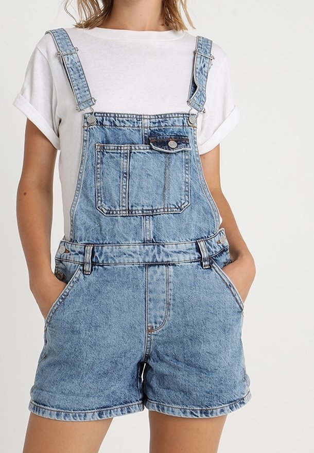 Ljusblå denimöveraller med justerbara axelband, framficka och sidofickor, i kombination med en vit t-shirt.