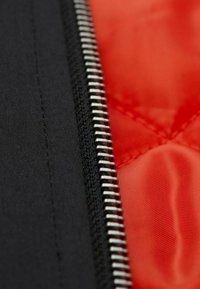 Schwarzer Stoff mit einem silbernen Reißverschluss-Detail und einem lebhaften roten Innenfutter, das eine gesteppte Textur zeigt.