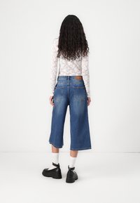 Culoți din denim de culoare albastru deschis, cu o croială lejeră, având două buzunare la spate și o etichetă din piele maro la talie. Top din dantelă cu mânecă lungă.